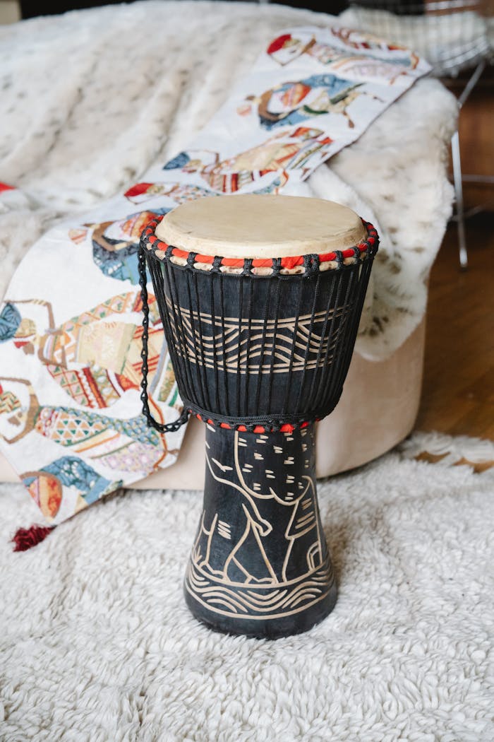 A decorative African djembe drum resting on a textured rug with a colorful blanket.