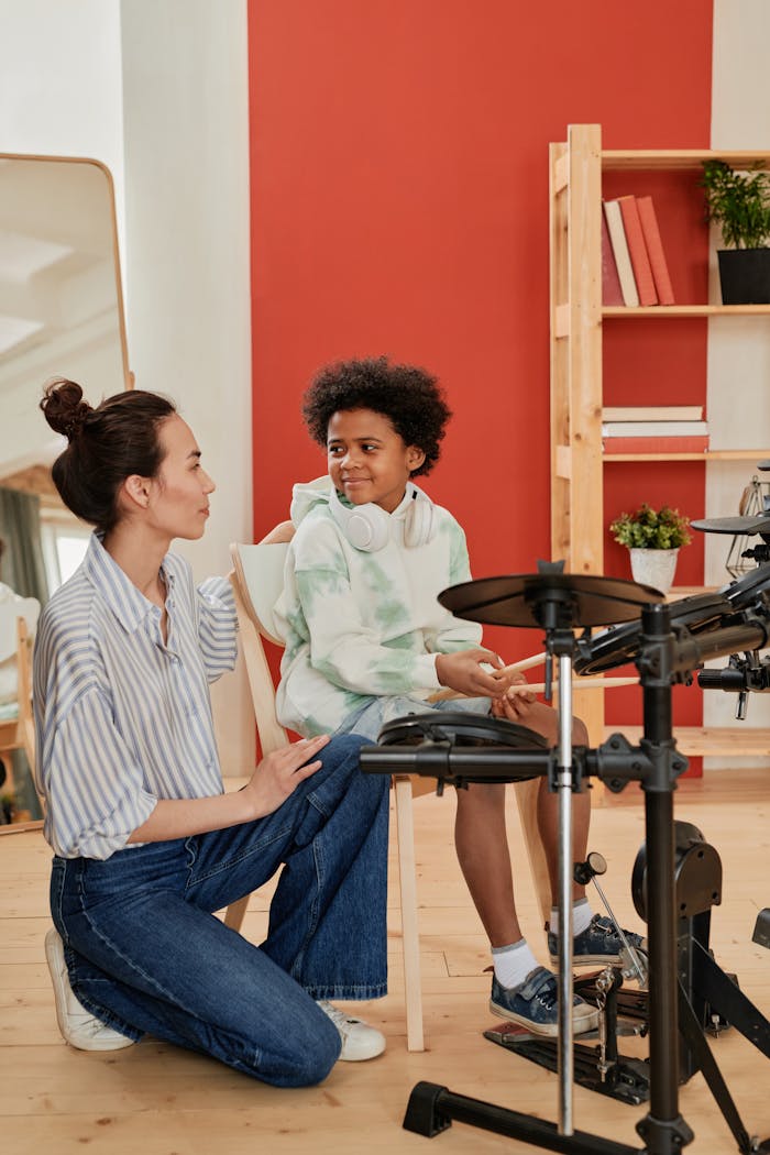 Boy learning to play electronic drums with a female instructor at home for music education.